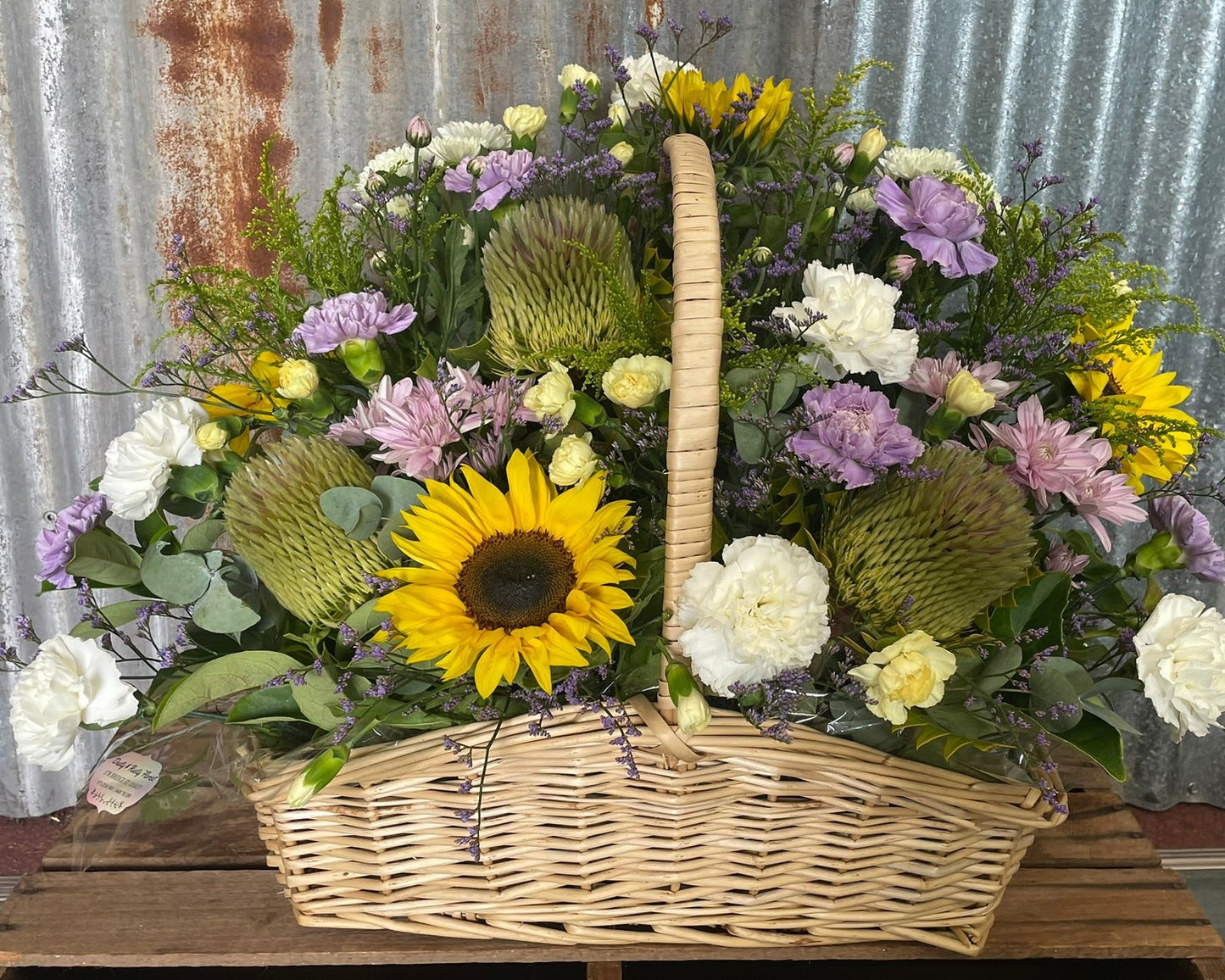 Floral arrangement in a wicker basket against a rustic metal wall.