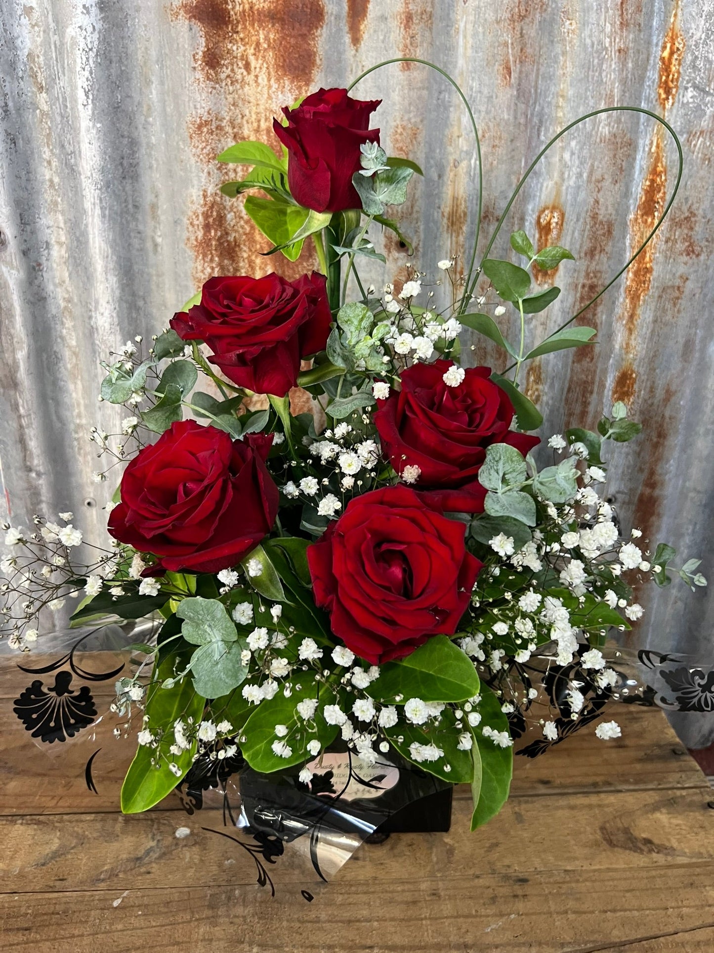 Arrangement of dark red roses with greenery on a rustic metal and wooden surface