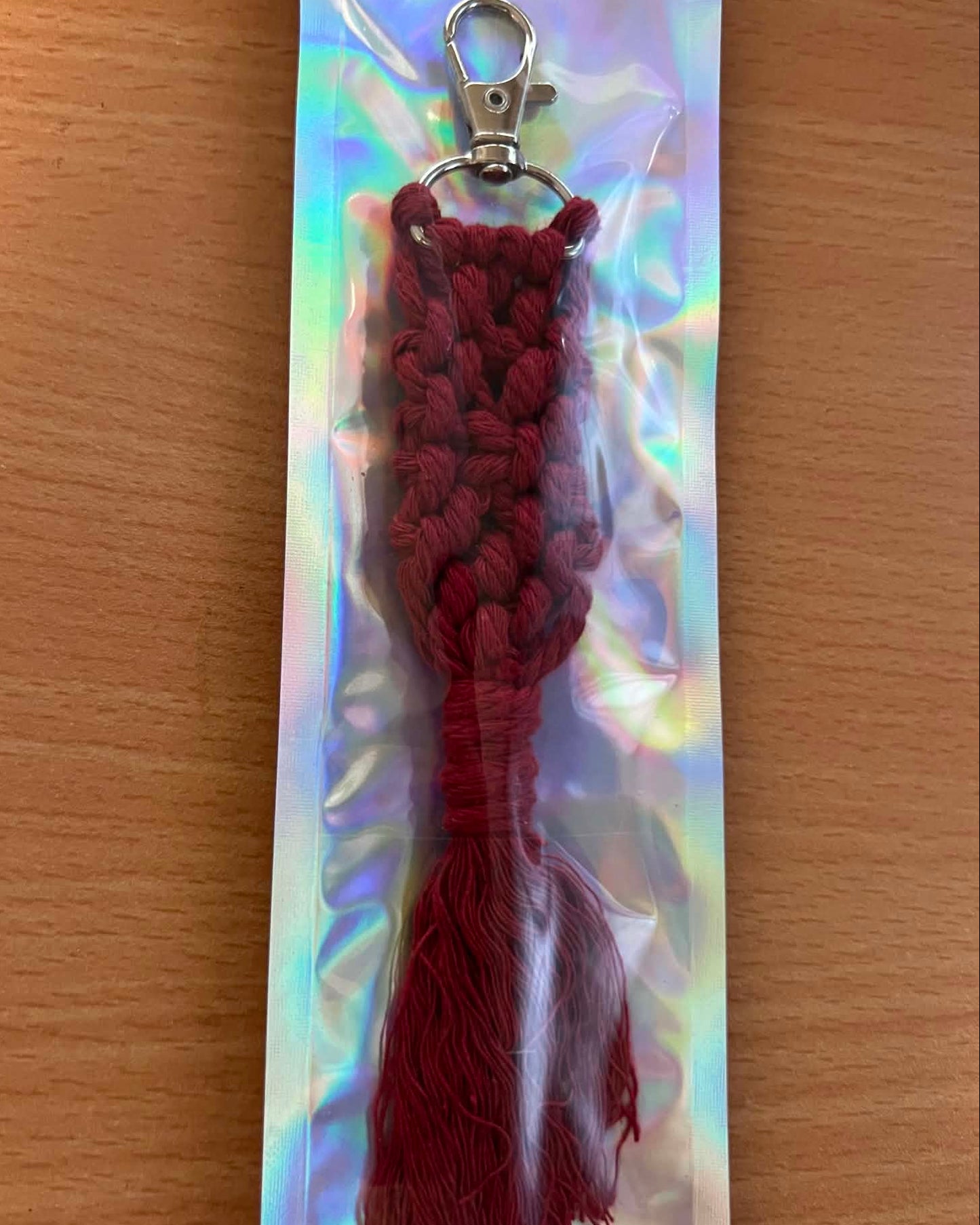 Burgundy braided keychain on a reflective card with a wooden surface background