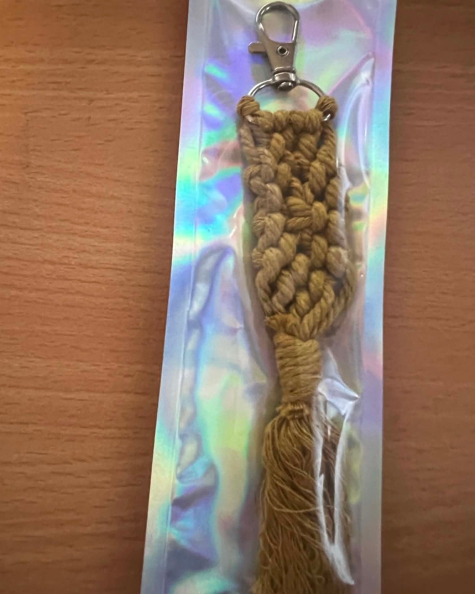 Coffee coloured Macrame keychain on a reflective card with a wooden background