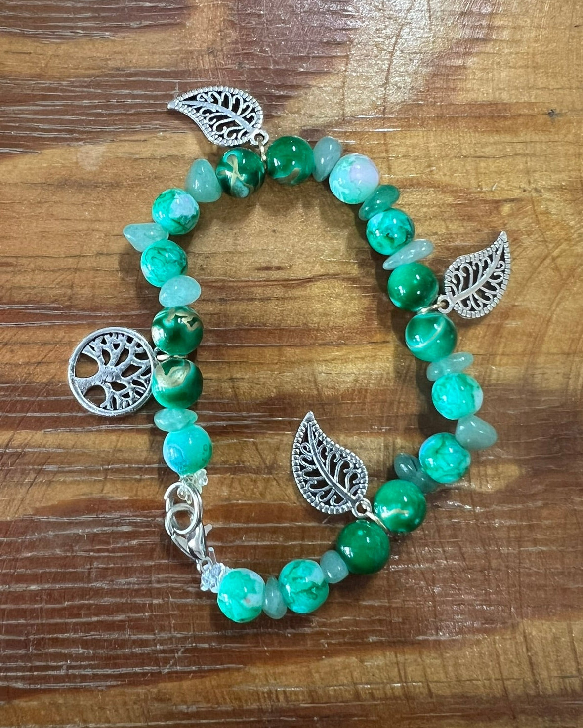 Green beaded bracelet with silver leaf charms on a wooden surface