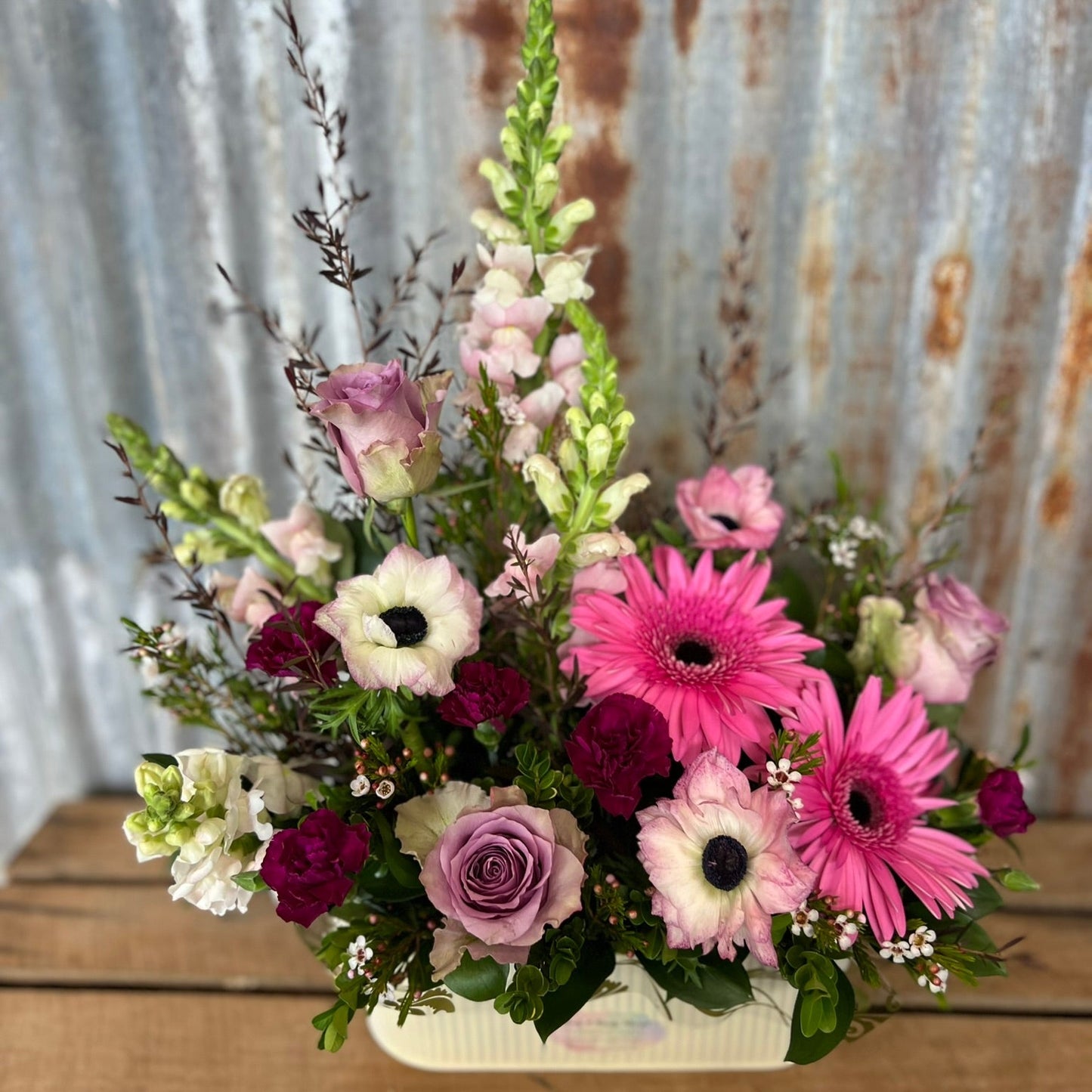 Floral arrangement with pink, white, and purple flowers on a wooden surface with a rustic metal background.