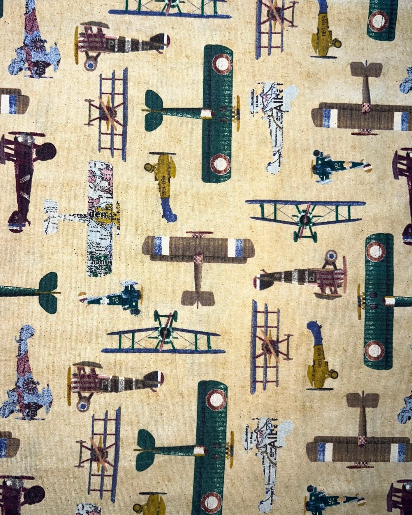 Vintage-style fabric pattern featuring multiple illustrated biplanes and a few small figures on a warm beige background.
